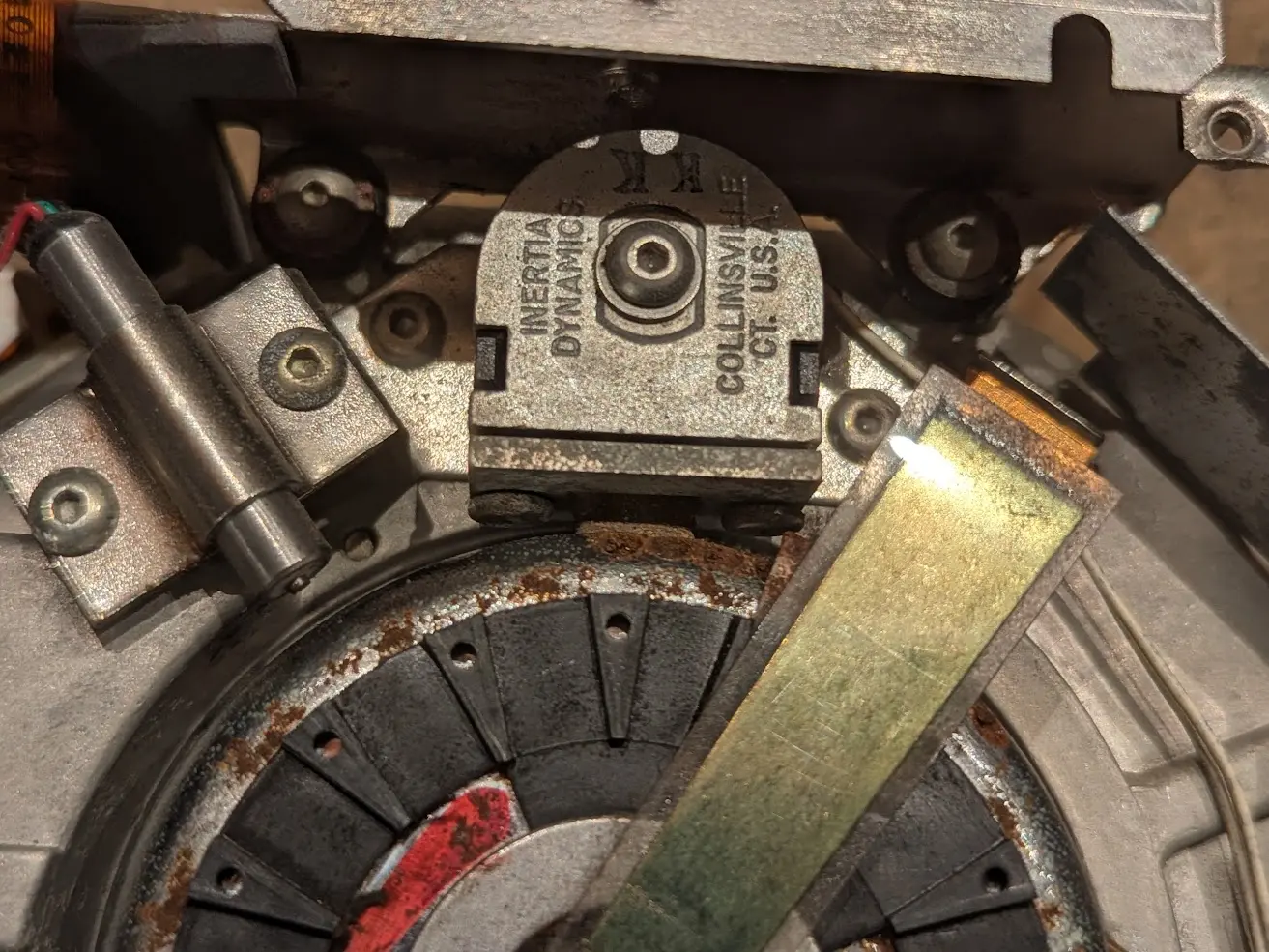 slightly rusty motor rotor with a ground strap leading to the center. above it is a solenoid with some sort of tiny retractable brake pad.