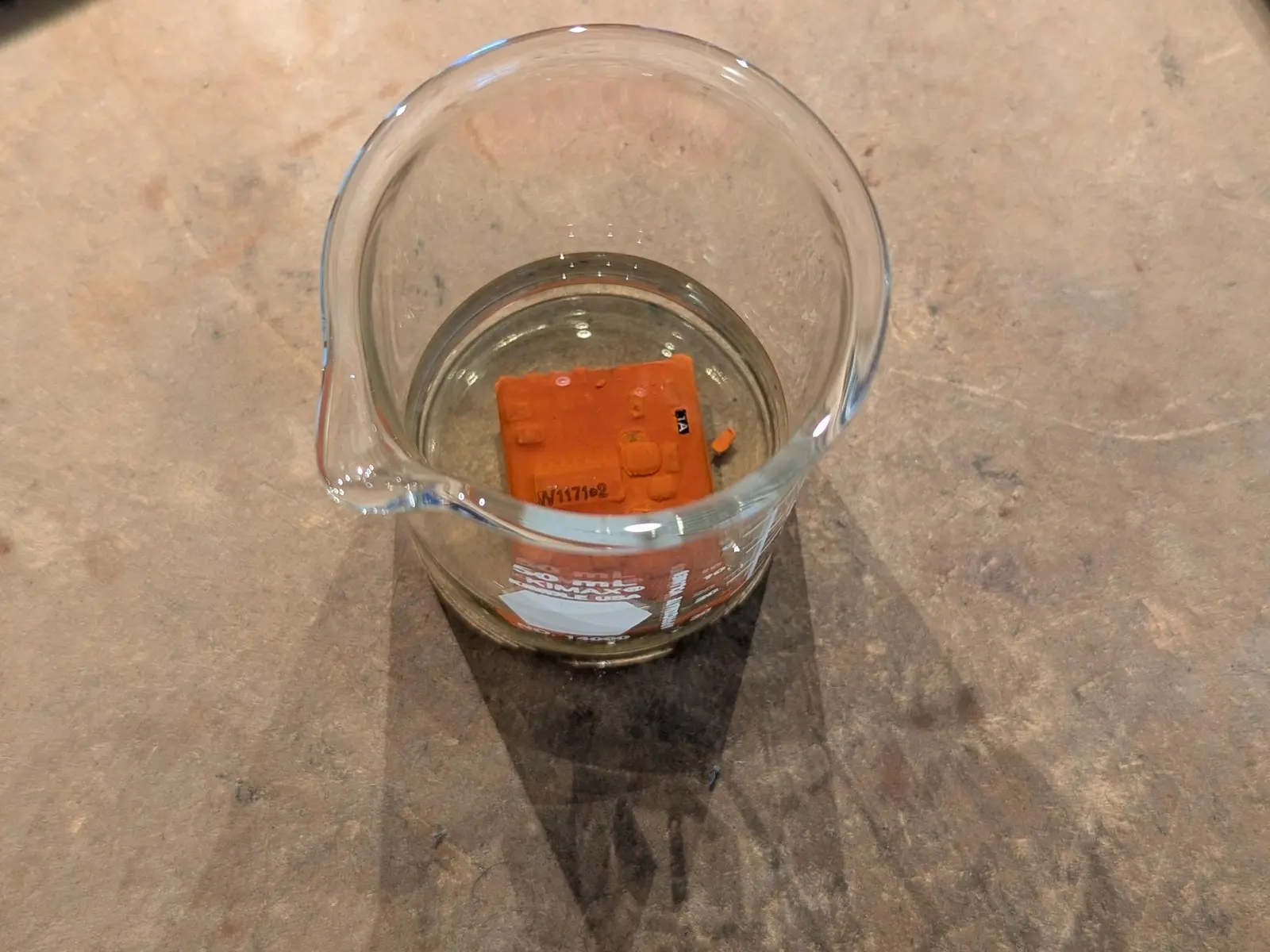 the module submerged in acetone inside a tiny glass breaker. part of the brown potting compound has fallen off revealing a sot-23 transistor marked "1A".