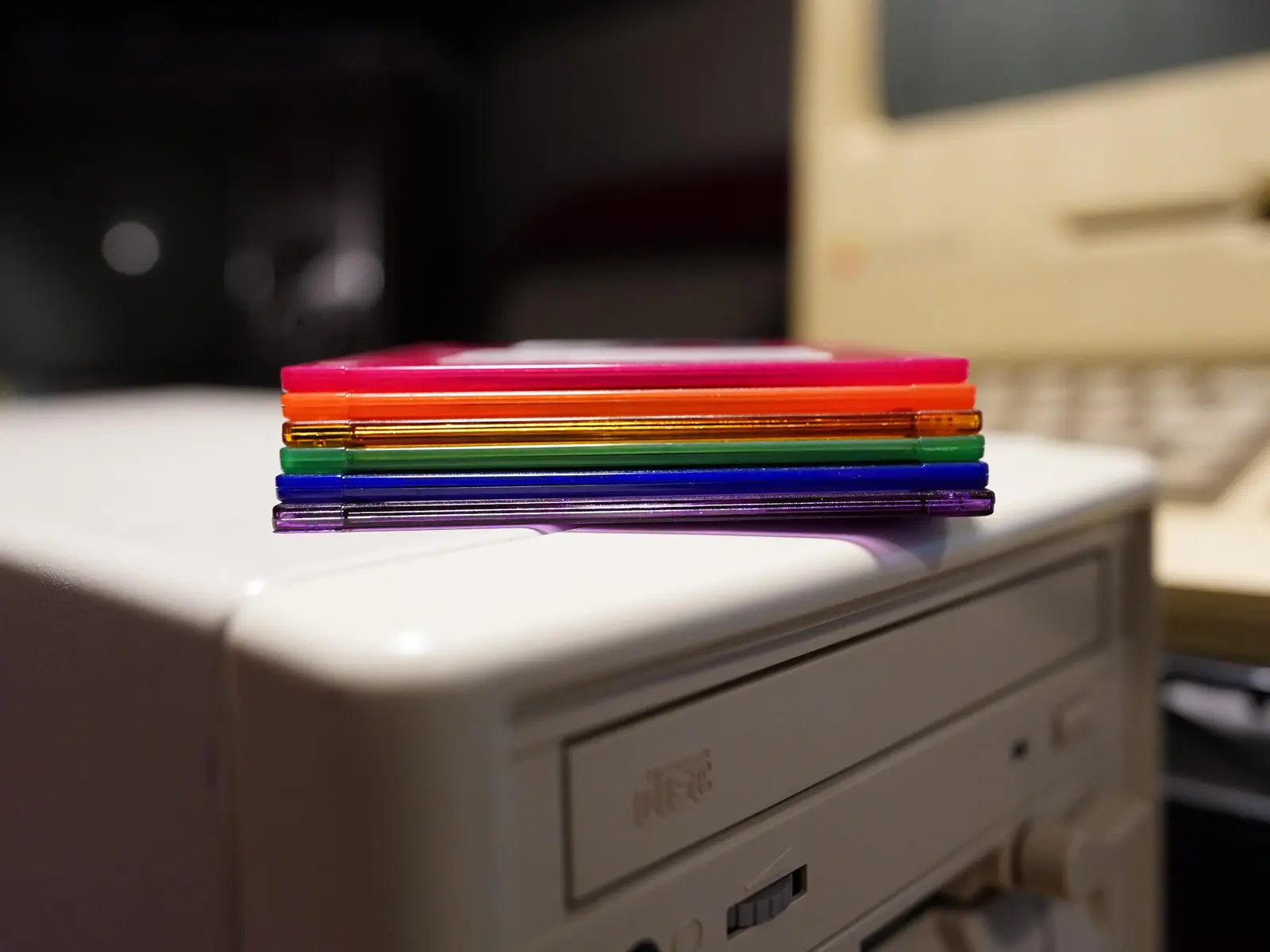 Six 3½" floppy disks in translucent Pride colors stacked atop a baby AT case. A CD-ROM drive and a 5¼" disk drive are partially visible, as is a Mac Plus blurred in the background.

The red, orange, green and blue disks are Imation, the purple and yellow are Memorex Cool Disks. In retrospect, the yellow of the Memorex is a little too sickly and drab compared to Imation's own neon yellow disk.