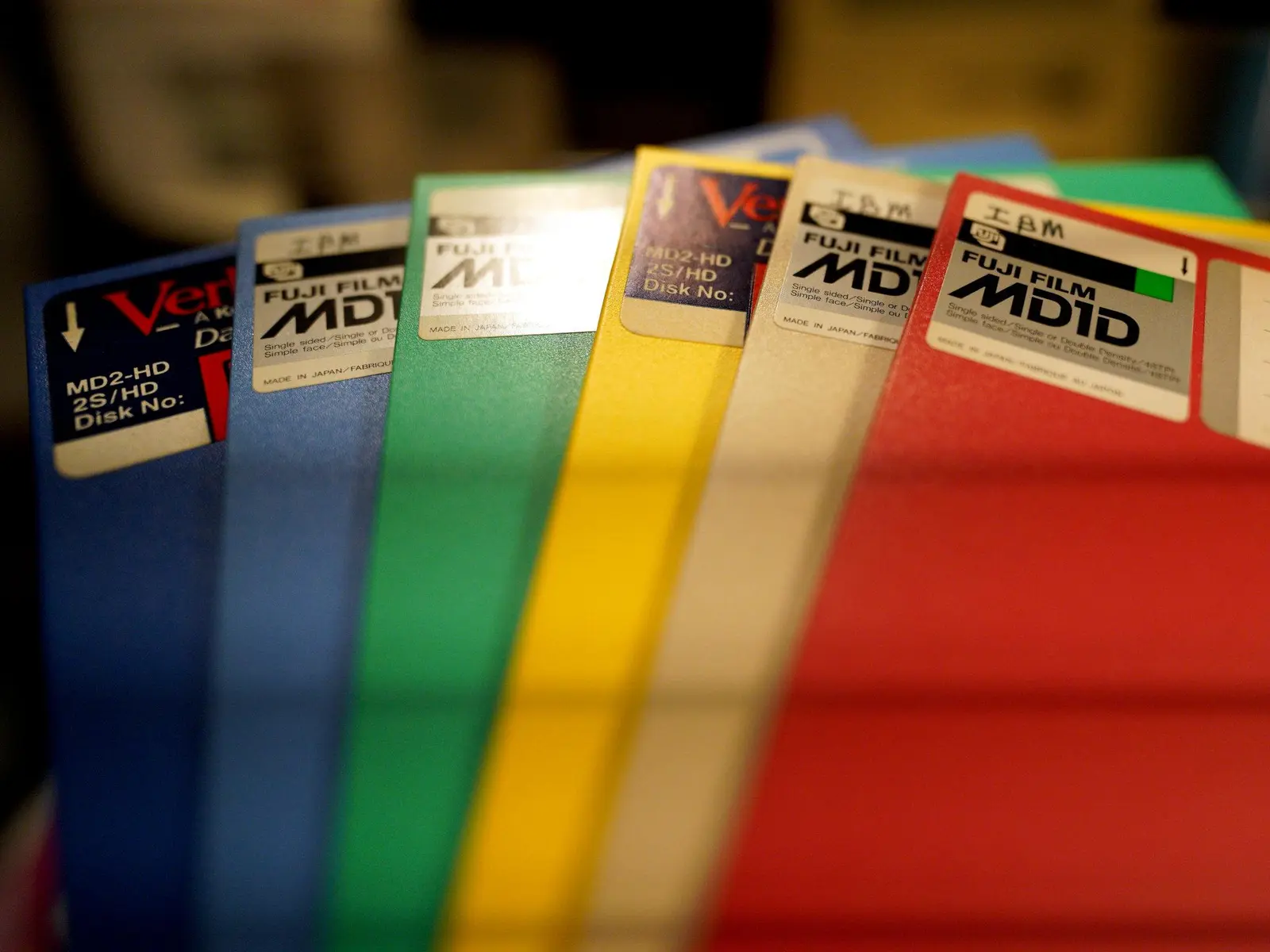 Six 5¼" floppy disks fanned out like a hand of cards.

The dark blue (standing in for purple) and yellow disks are high-density Verbatim media, while the light blue, green (more turquoise, but as close as I could get), beige (very very pale orange?) and red are single-density Fujifilm.

Annoyingly, there are bands across the photo, because apparently I have a fluorescent bulb nearby...