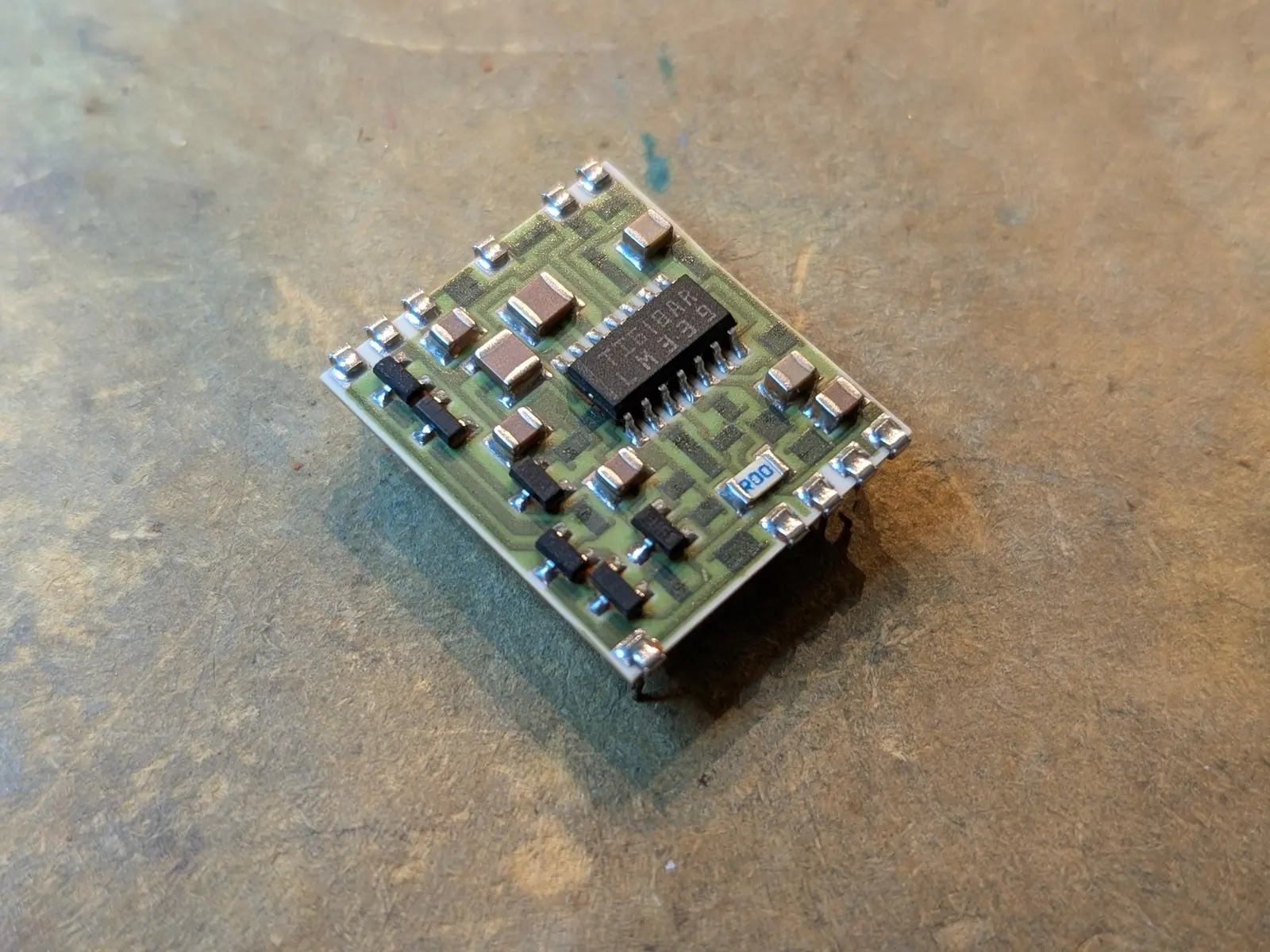 white ceramic board with light green mask and trace, with dark rectangles. clipped to the edge are some soldered pins.