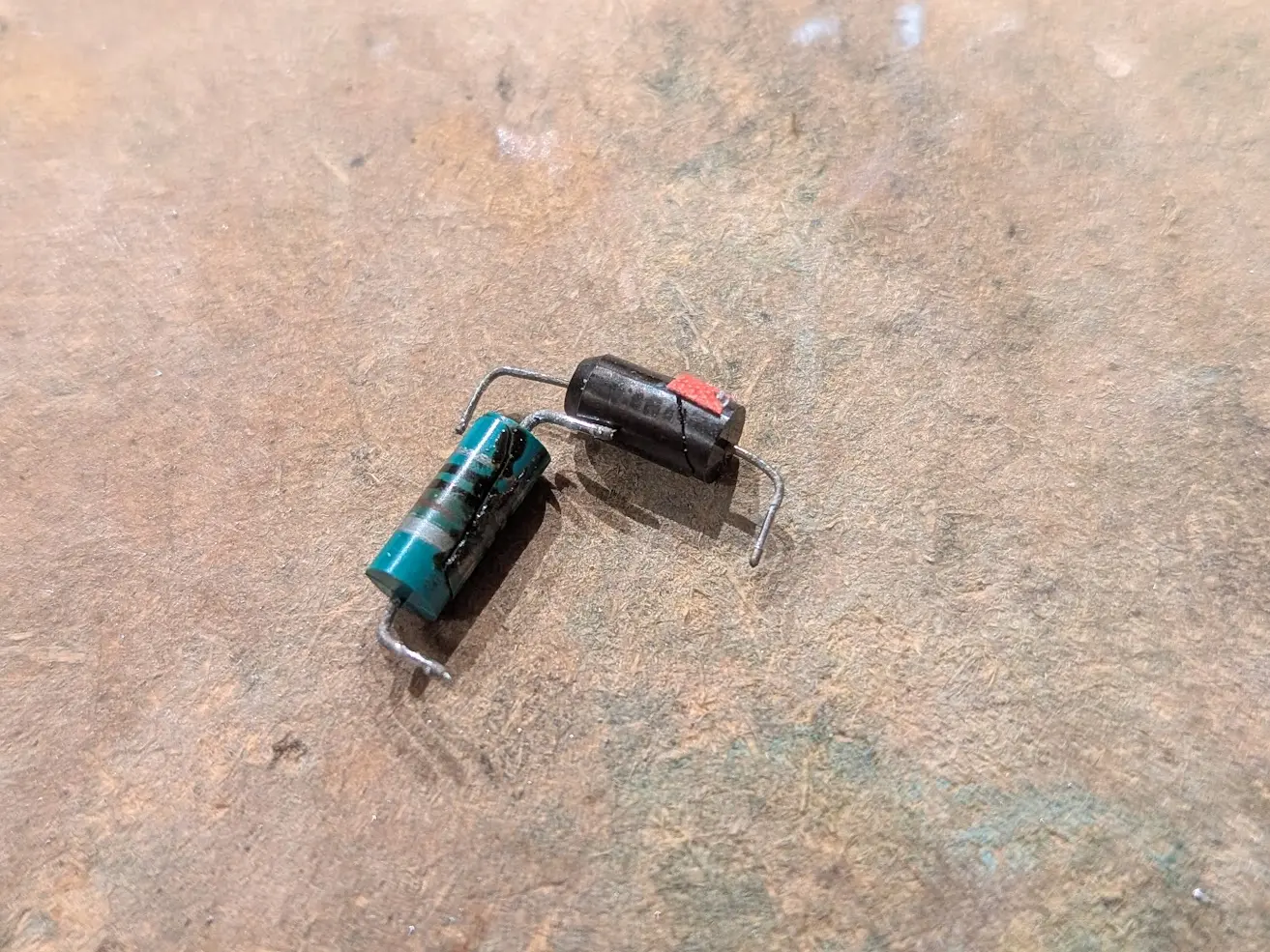 two axial components slightly larger than a 1/2 watt resistor. one is a bullet shaped black tantalum capacitor with a huge crack. the other is a resistor-style inductor marked with brown, black black (10uH). it has a crack exuding some sort of toxic goo