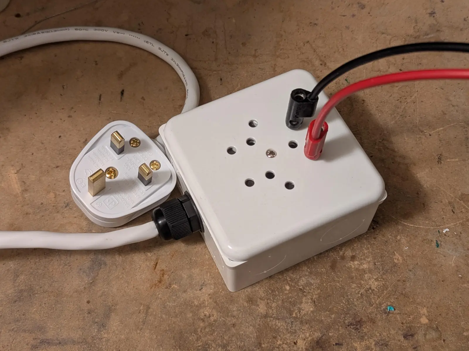 British plug with a wire going to a 86mm electrical box with a Swiss triple 3-pin outlet that is now illegal there because it isn't recessed. two banana cables are plugged into one of the outlets.